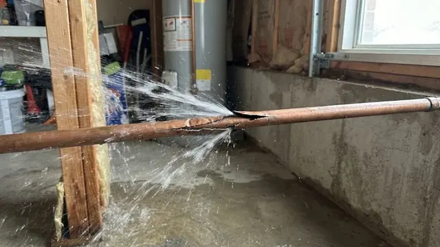 Split copper pipe spraying water across a flooded basement beside a water heater