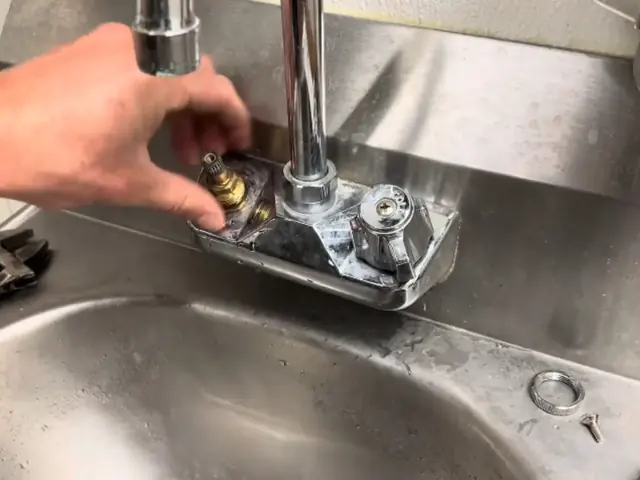 Hands replacing the cartridge on a chrome faucet mounted on a stainless steel sink